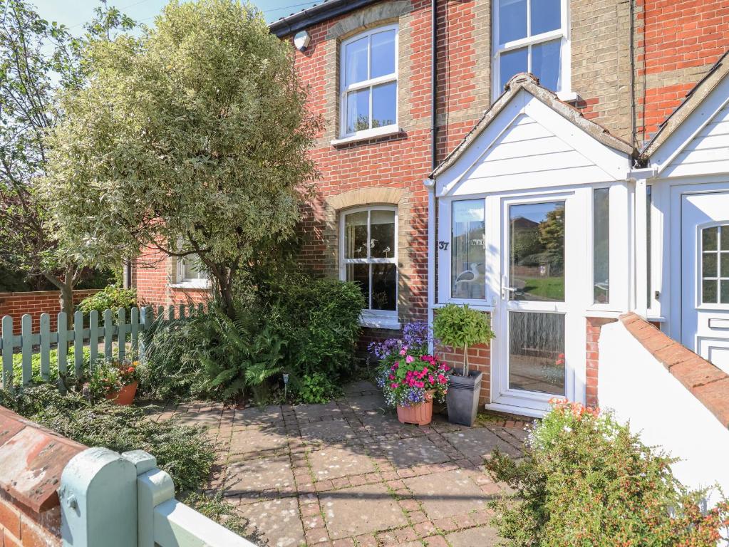 front garden of brick house with white porch, potted flowers, small tree, and green picket fence