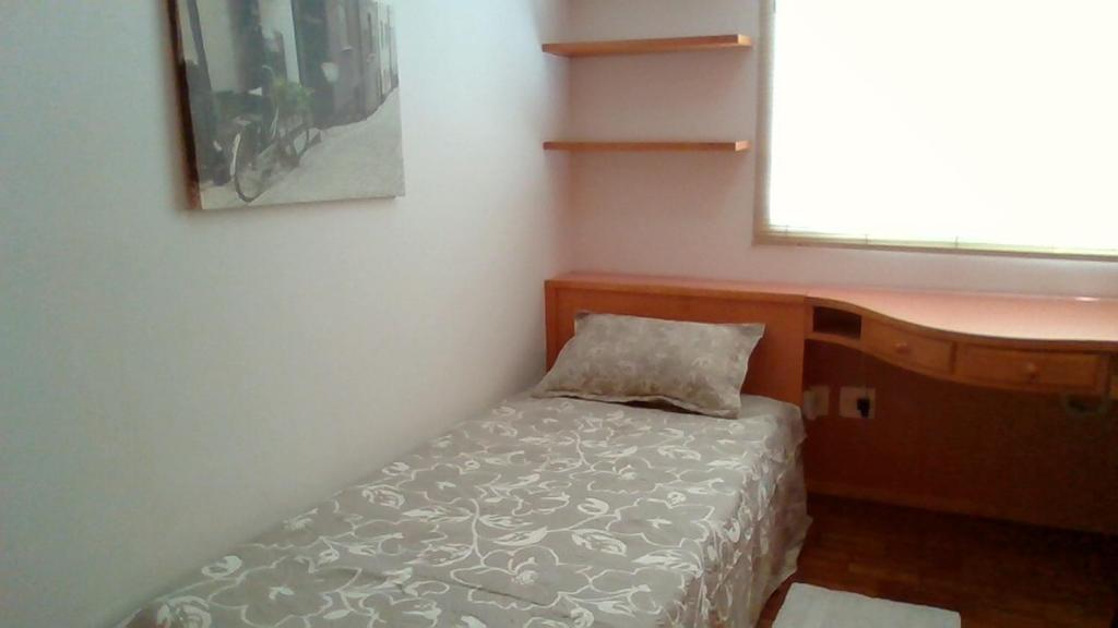 um pequeno quarto com uma cama e uma janela em Aconchego bem localizado em Varginha