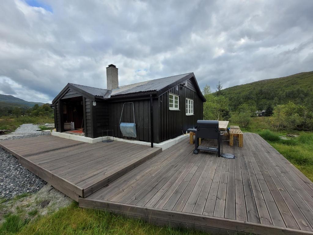 eine schwarze Hütte mit einer Holzterrasse und einem Schreibtisch in der Unterkunft Tangen - cabin with 4 bedrooms - great nature in Norheimsund