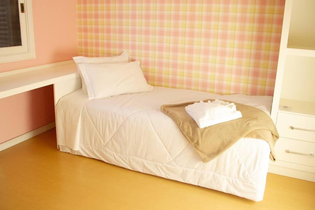 uma pequena cama com lençóis brancos e almofadas em Casa Felice - Canela em Canela