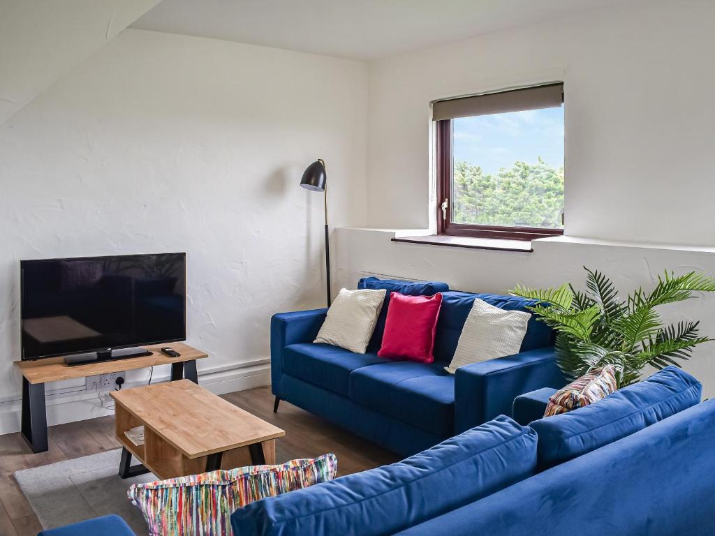 a living room with a blue couch and a tv at Sandymouth Cottage in Marhamchurch