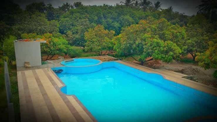 een groot blauw zwembad met bomen op de achtergrond bij Capital O Murlidhar Farm Jamnavad in Junagadh