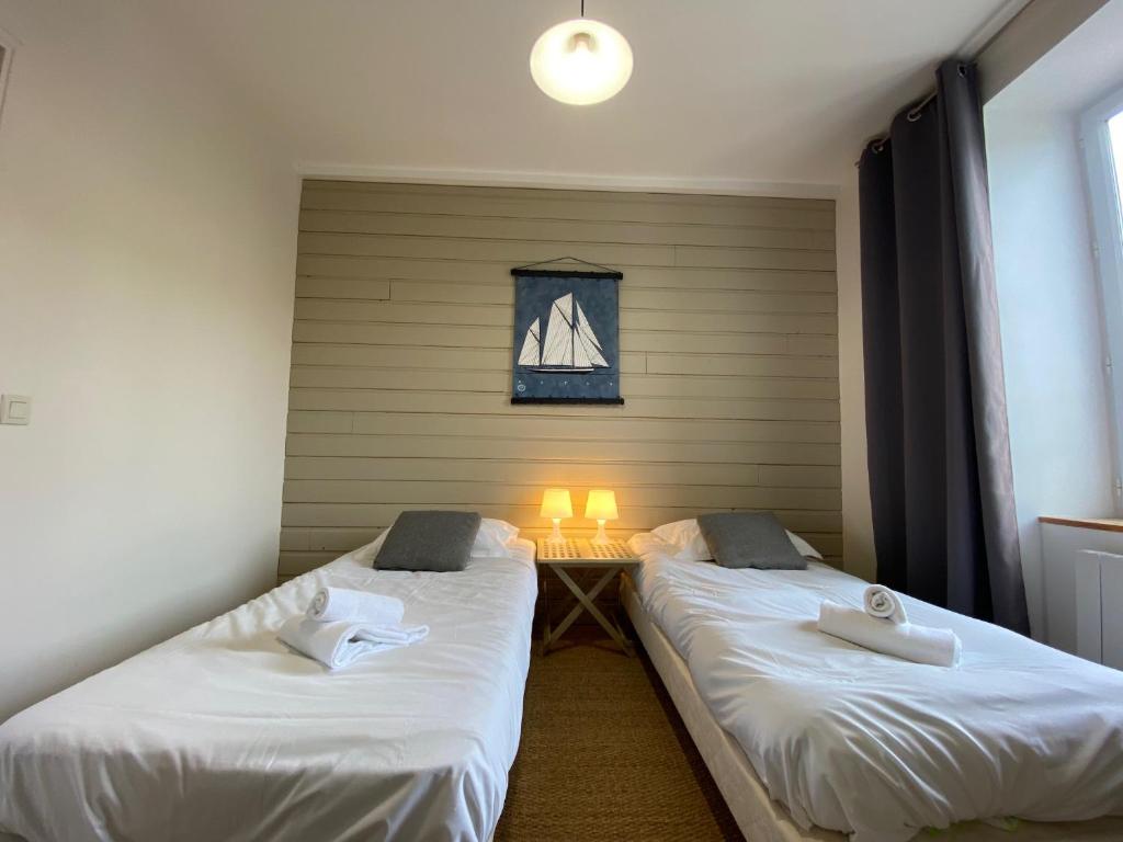 two beds in a room with a table and a window at Le Château de Sable in Plougasnou