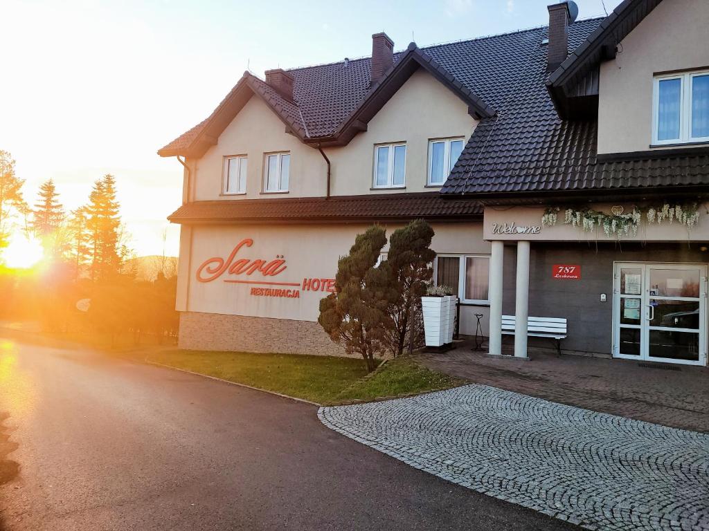 a house with the sun setting in front of it at Hotel Restauracja Sara in Laskowa