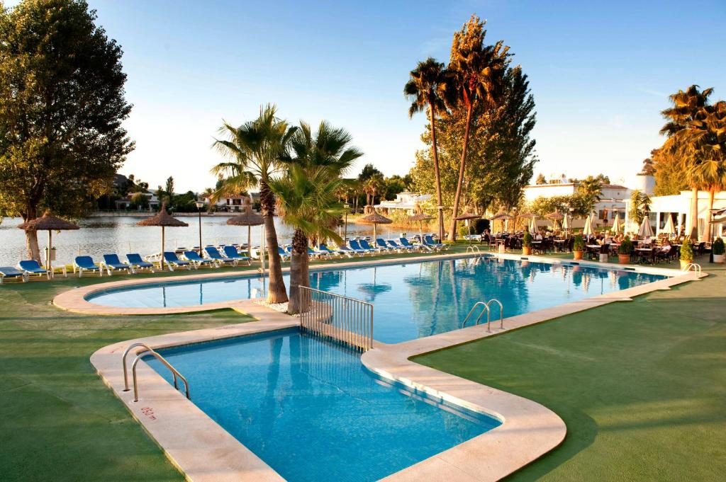 a swimming pool at a resort with palm trees and chairs at Grupotel Amapola in Playa de Muro