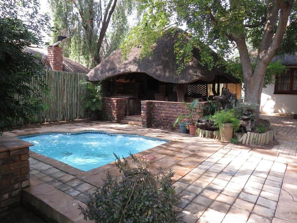 een achtertuin met een klein zwembad met een rieten dak bij Harties Lodge - Private Suite in Hartbeespoort