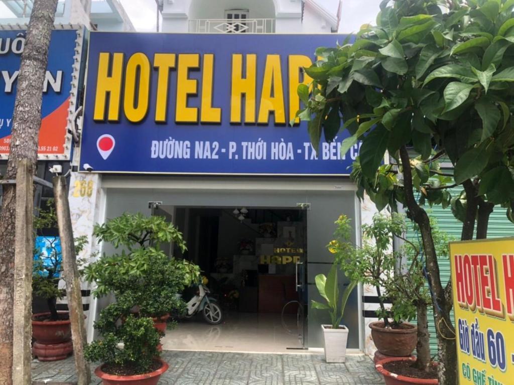 Happy 1 Hotel Binh Duong في Bến Cát: علامة لفندق hacienda مع النباتات في الأمام