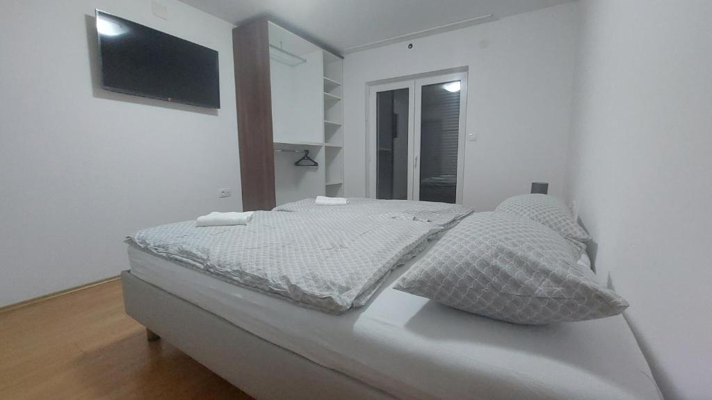 a bed in a white room with a tv on the wall at Apartman i Sobe Vasilić in Jurandvor