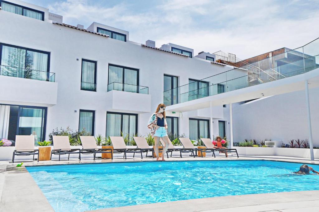 een vrouw die naast een zwembad voor een gebouw staat bij Pêro Teive Bay Apartments Hotel in Ponta Delgada