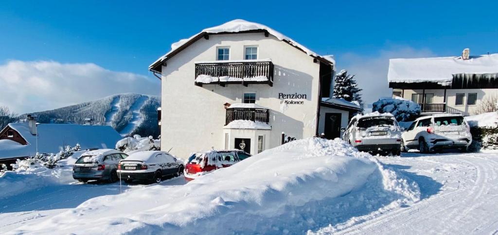 a building with cars parked in a parking lot covered in snow at Penzion V Kolonce in Strážné