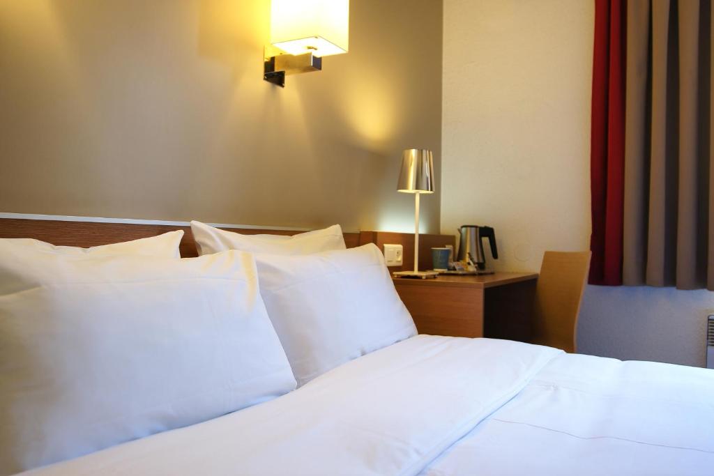 1 dormitorio con cama con almohadas blancas y escritorio en Kyriad Le Bourget Centre- Parc Des Expositions, en Le Bourget