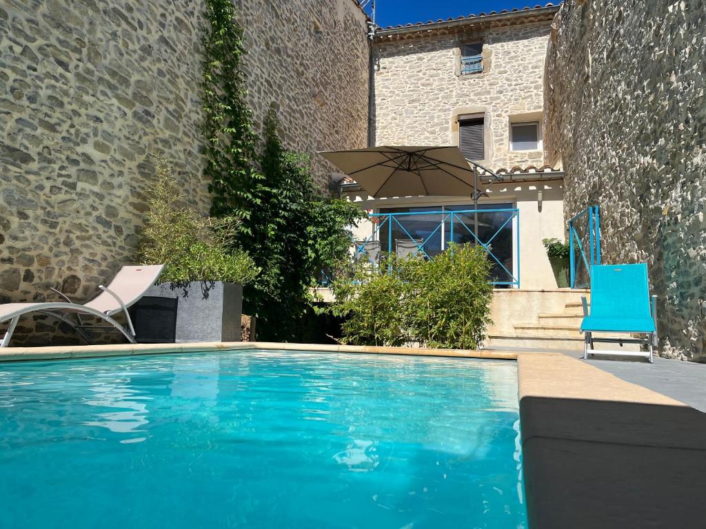 une piscine avec deux chaises et un parasol dans l'établissement Chez Elia, pour les amoureux des vieilles pierres, à Cesseras