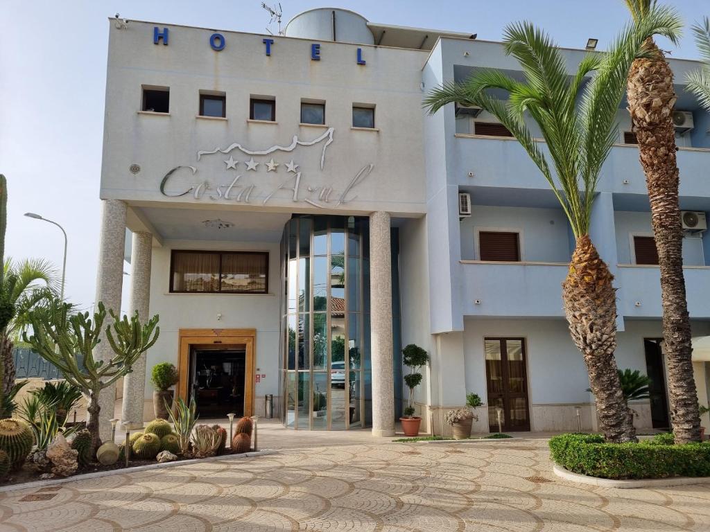 a white building with palm trees in front of it at Hotel Costa Azul in Balestrate