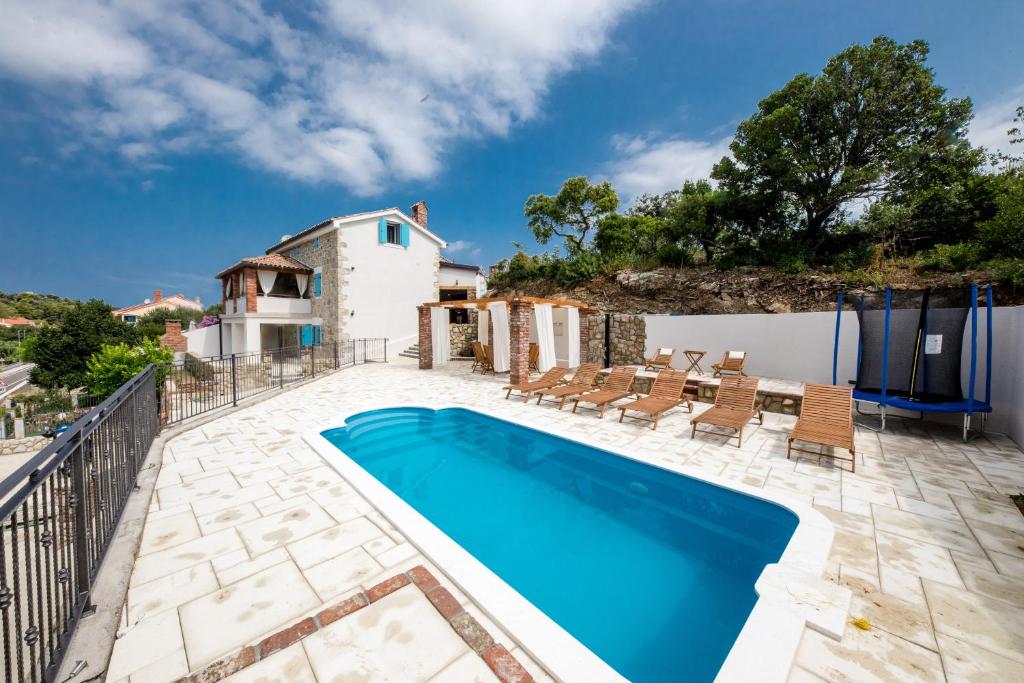 a swimming pool with chairs and a house at Villa Copun with heated pool in Rab