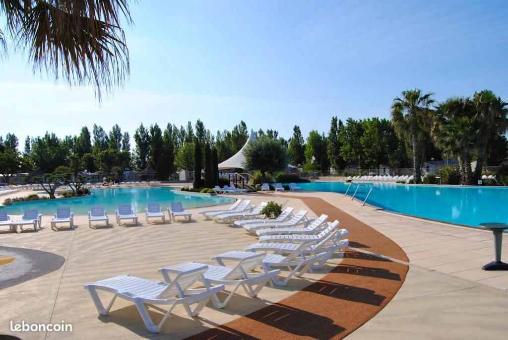 a row of white lounge chairs next to a swimming pool at Bungalow de 3 chambres avec piscine partagee et terrasse a Vias a 1 km de la plage in Vias