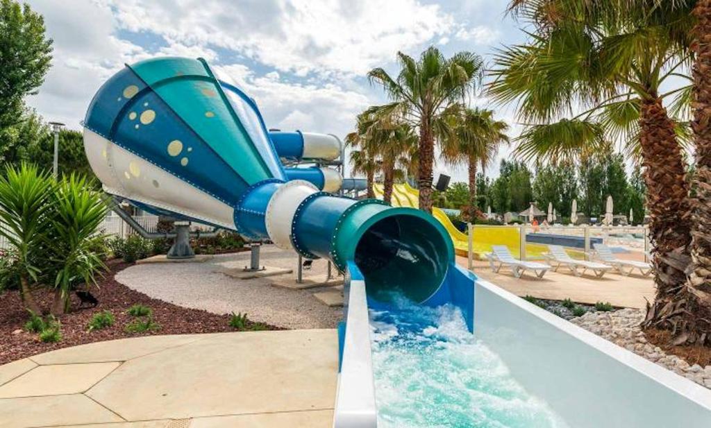 a blue slide in a water park with palm trees at Bungalow de 3 chambres avec piscine partagee et terrasse a Vias a 1 km de la plage in Vias