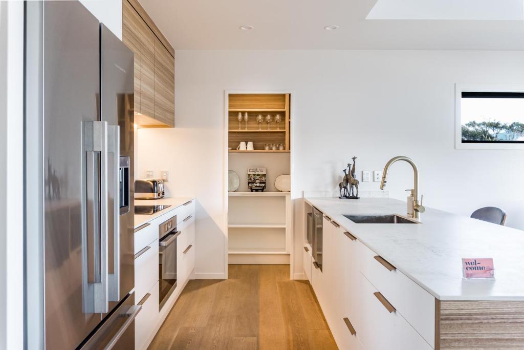 a kitchen with white cabinets and a stainless steel refrigerator at Okiwi Landing in Raglan