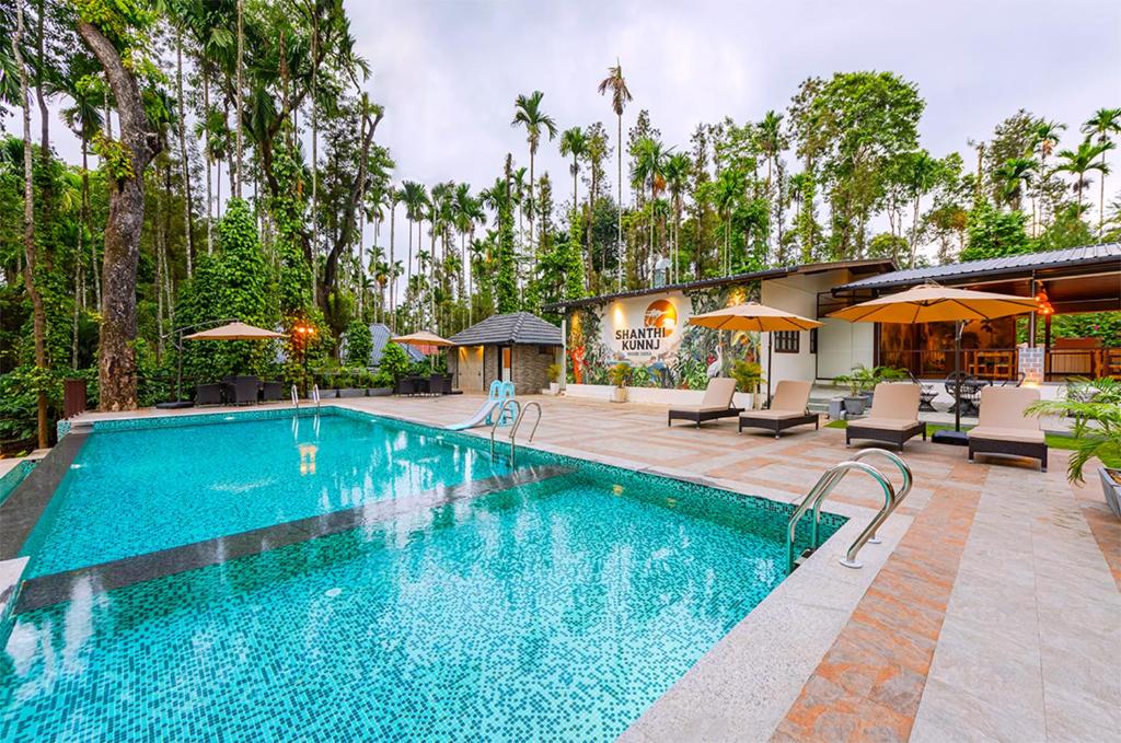 Una piscina con sillas y sombrillas al lado de una casa. en Shanthi Kunnj Riverside Exotica Chikmagalur, en Chikmagalur