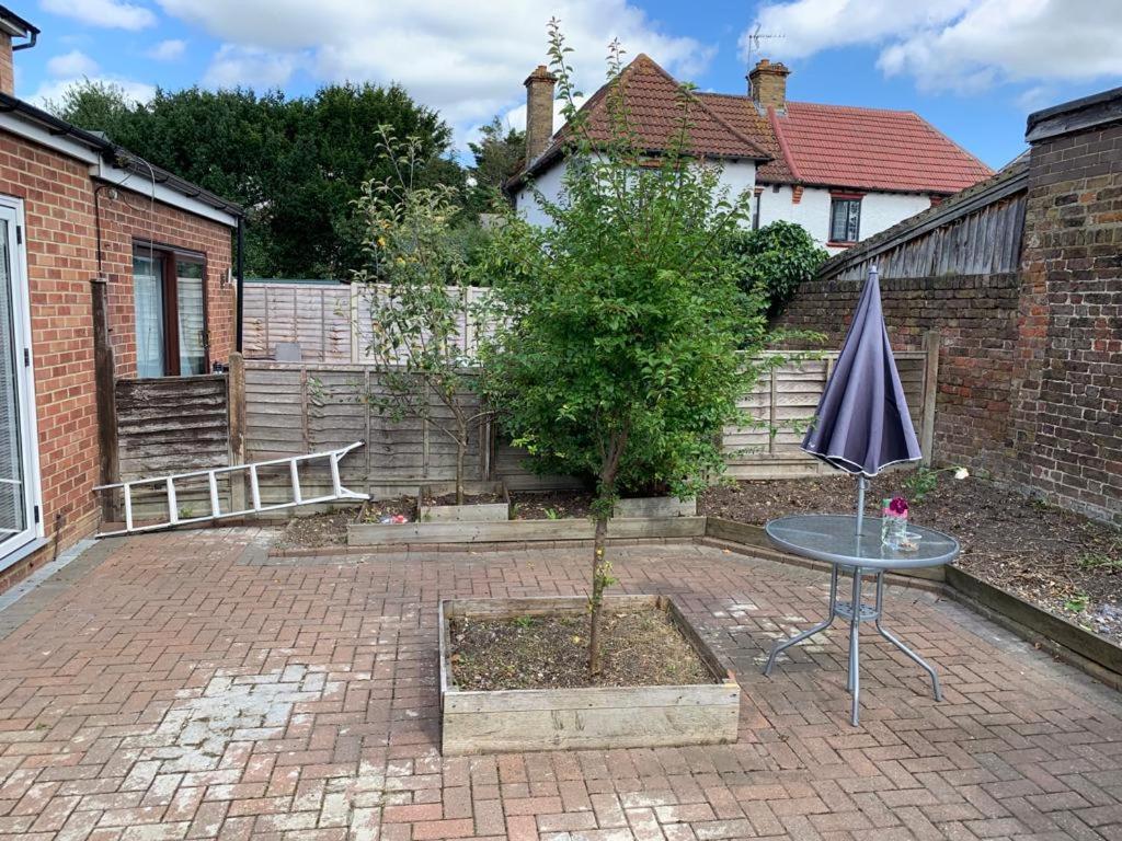 a table with an umbrella and a tree in a yard at Cambridge Suites in Harmondsworth