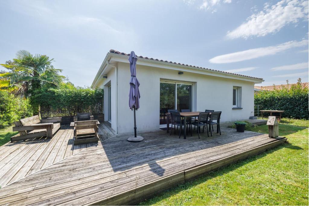 eine Holzterrasse mit einem Tisch, Stühlen und einem Sonnenschirm in der Unterkunft L Entre2mers in Sadirac