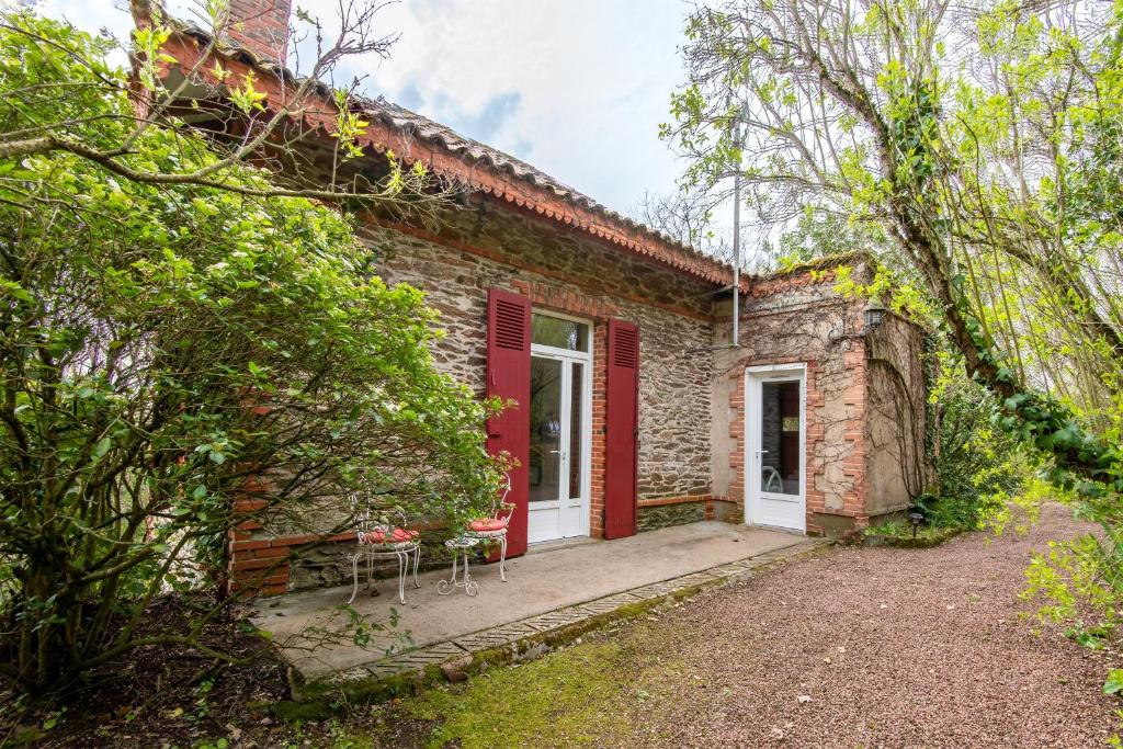 une maison en briques avec une porte rouge et deux chaises dans l'établissement L'Écrin de Verdure - Pavillon avec piscine partagée, à Thouars