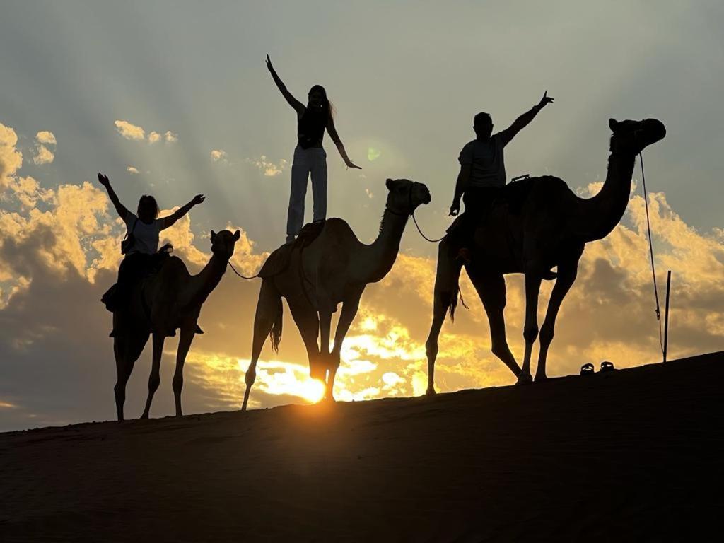 a group of people riding on camels on the beach at Oman desert private camp in Shāhiq