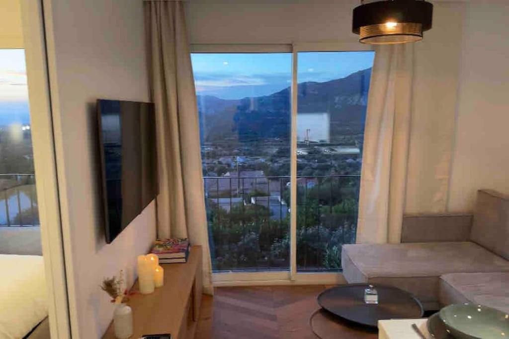 a living room with a couch and a large window at Appartement rénové entre terre et mer avec piscine in Calenzana