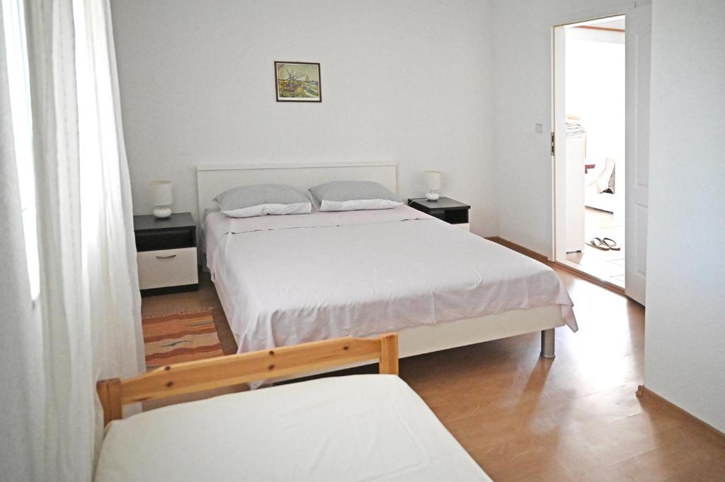 a white bedroom with two beds and a window at Apartments Antica in Vrboska