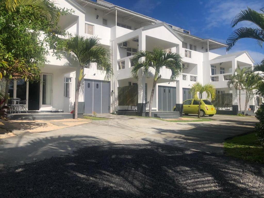a white apartment building with palm trees and a yellow car at Spacious Three Bedroom Apartment in Grand Gaube
