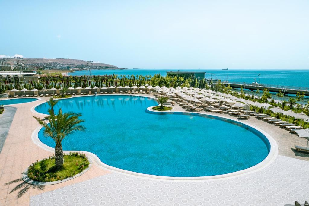 uma grande piscina com cadeiras e palmeiras e o oceano em Апартаменты у моря - в "Green City RESORT" em Baku