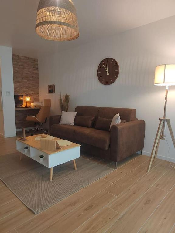 ein Wohnzimmer mit einem Sofa und einer Uhr an der Wand in der Unterkunft T2 balnéothérapie, jardin, parking, tram, boulodrome in Blagnac