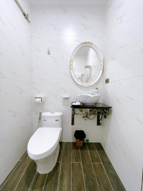a white bathroom with a toilet and a mirror at Paris Hotel & Cafe in Vĩnh Long