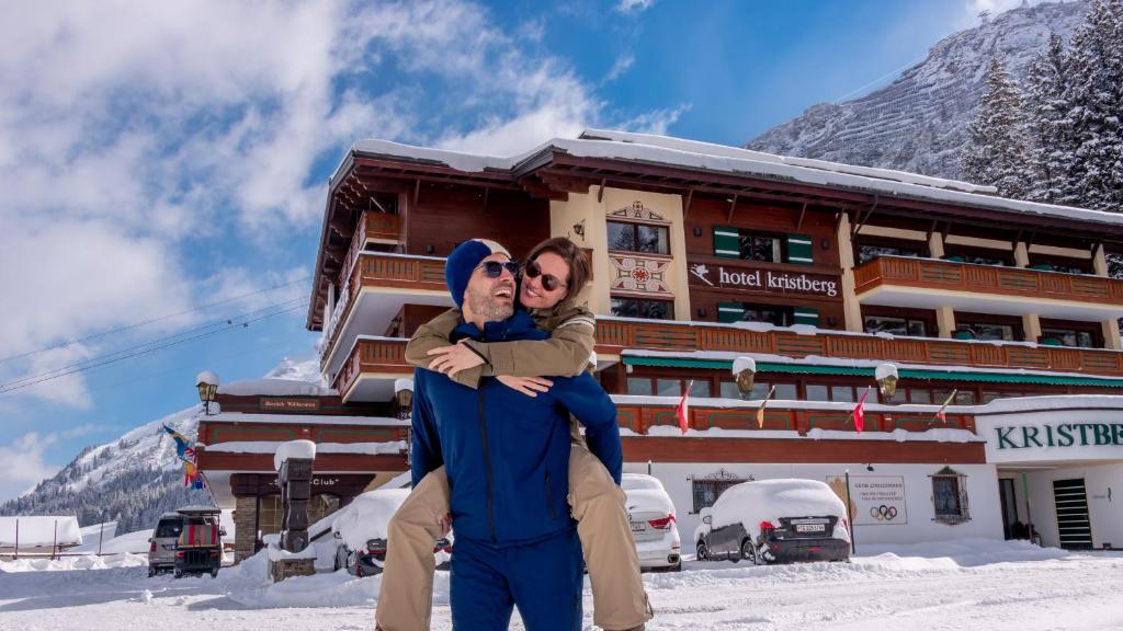 un hombre y una mujer parados en la nieve frente a un edificio en Hotel Kristberg en Lech am Arlberg