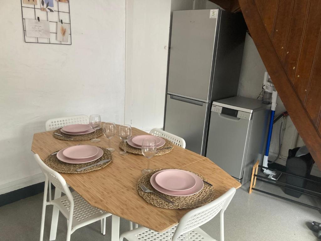 a wooden table with chairs and pink plates and a refrigerator at Charmante petite maison à Olne in Olne