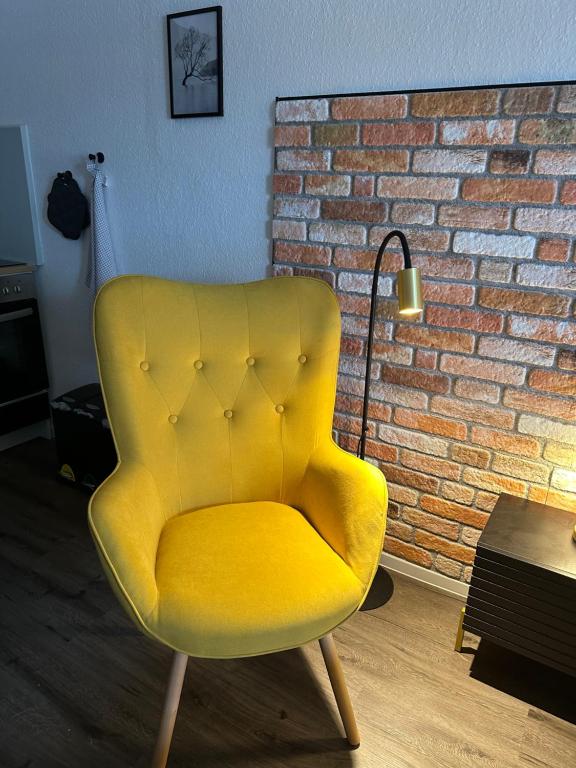 a yellow chair in a room with a brick wall at Moderne Ferienwohnung 5min vom Wasserschloss - Free WIFI & Netflix in Neukirchen