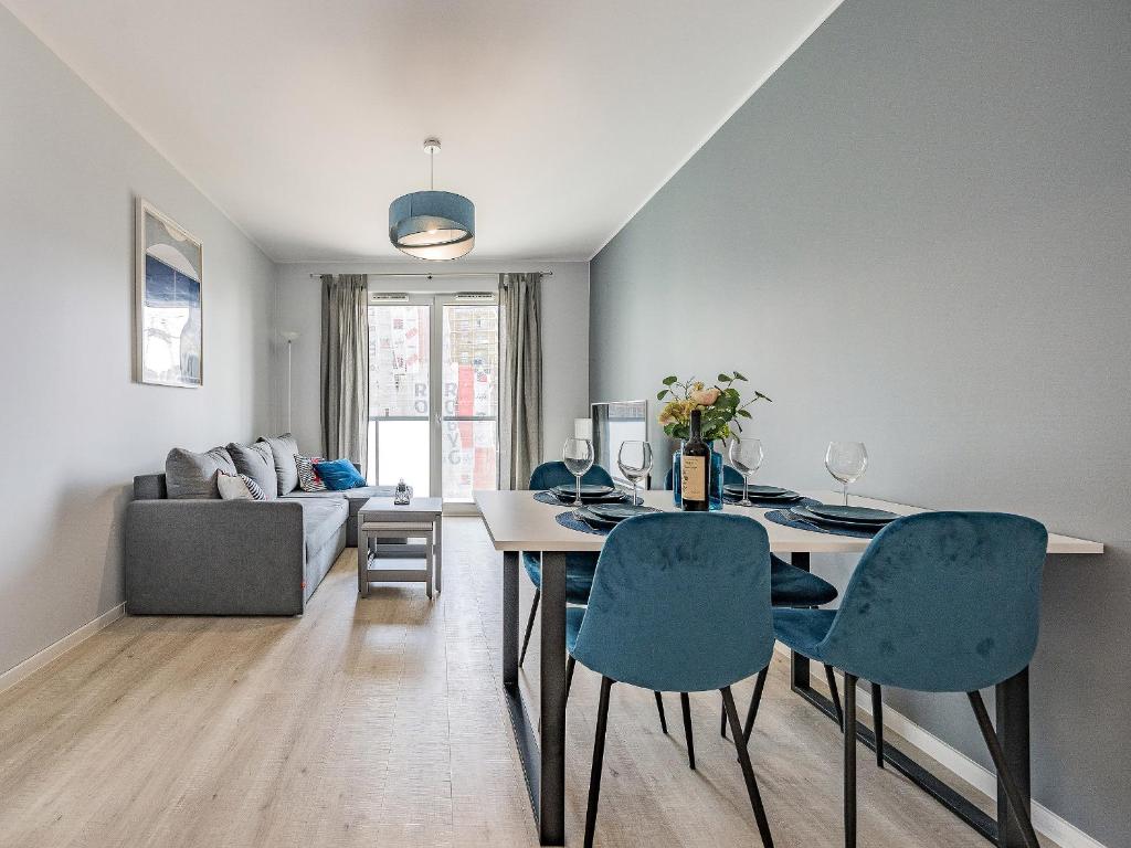 a living room with a dining room table and blue chairs at Hello Apartments Letnica with private parking in Gdańsk