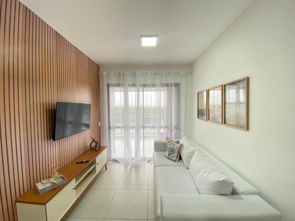 a living room with a white couch and a tv at TULUM Bertioga - belo apartamento com vista para o mar in Bertioga