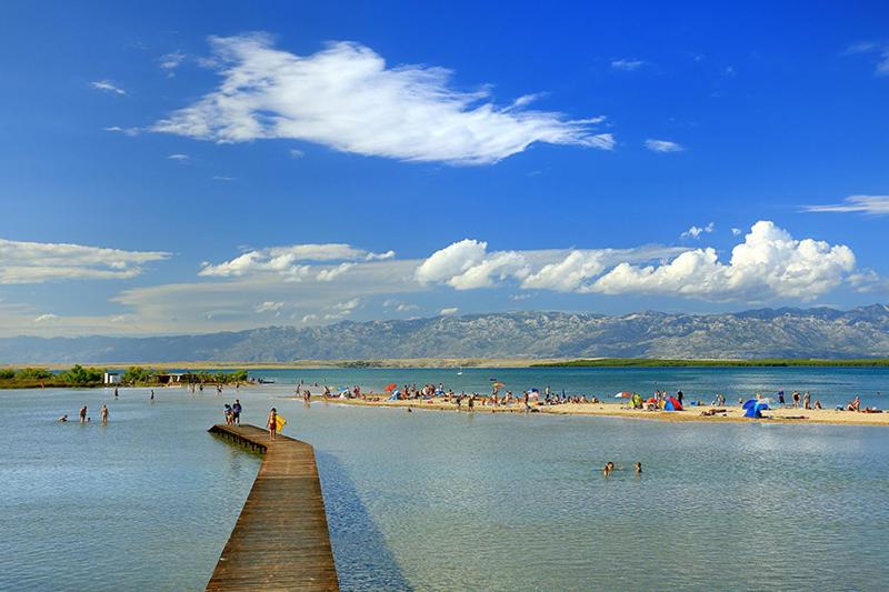 grupa ludzi na plaży z molo w obiekcie Apartments Gabriel w Nin