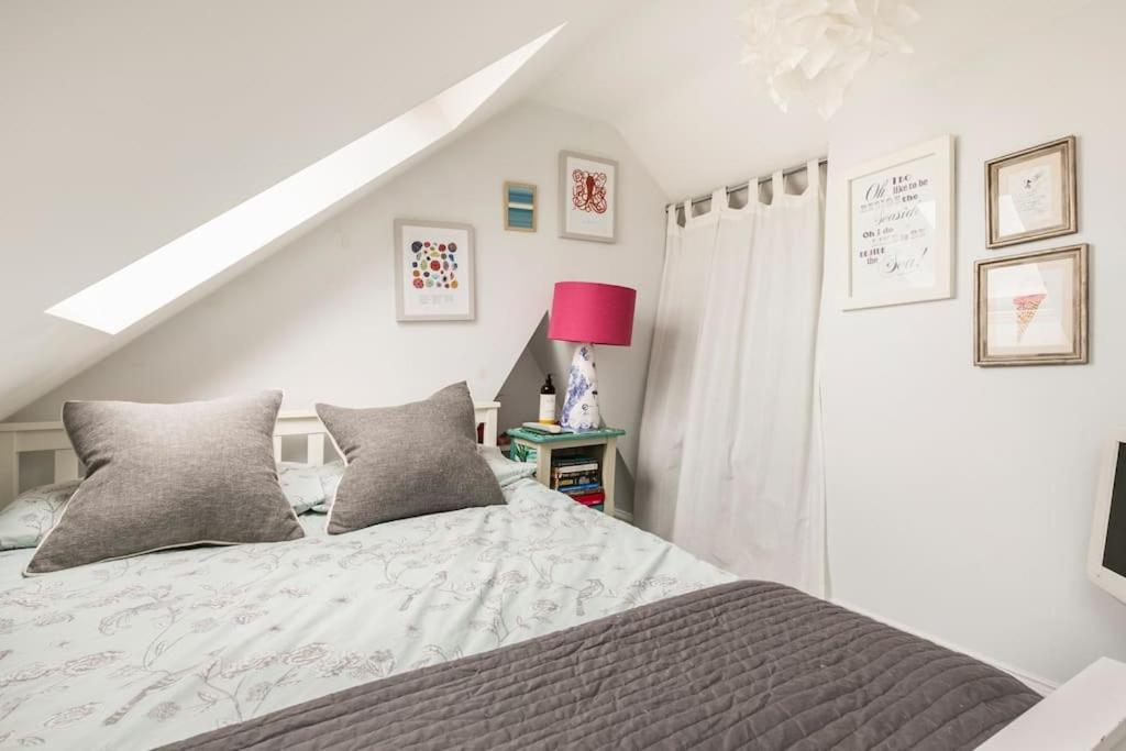 a white bedroom with a bed and a pink lamp at Hideaway Cottage - seaview room with shared bathroom in Sandgate