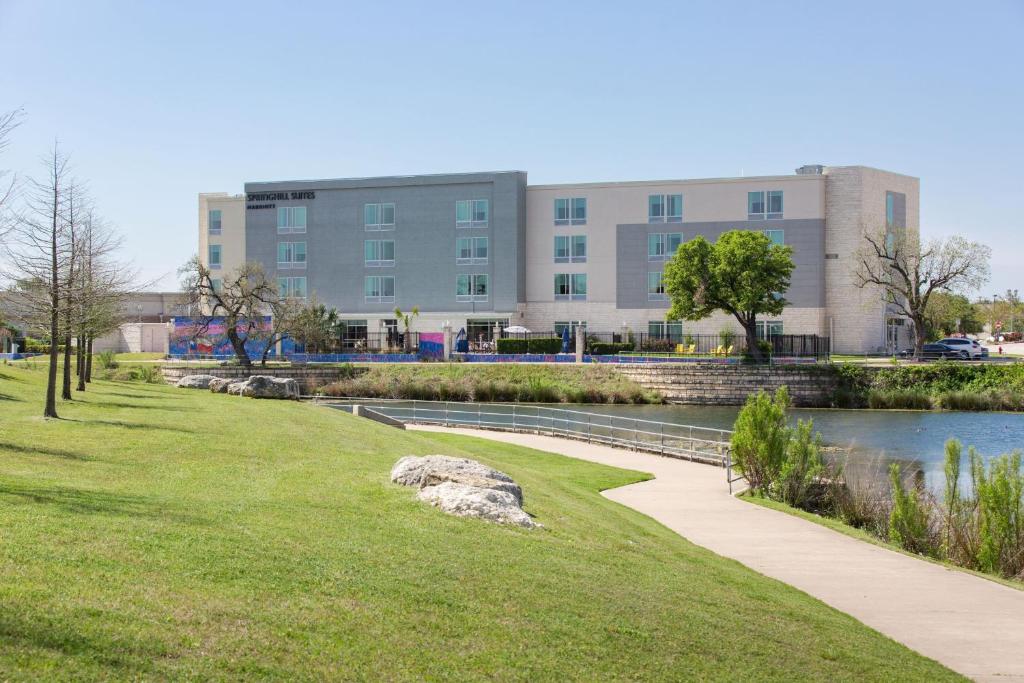 a building in the background of a park with a river at SpringHill Suites by Marriott Austin Cedar Park in Cedar Park