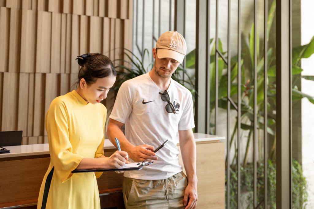 Two guests consult a staff member beside the hotel’s bright, plant-filled reception area.