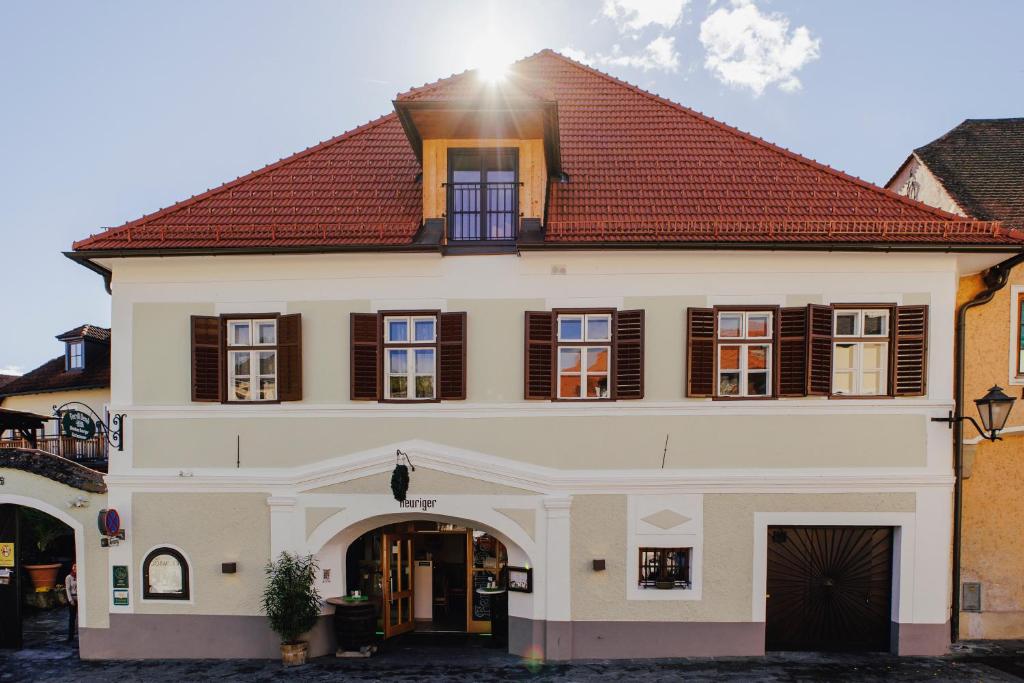 un grand bâtiment blanc avec un toit rouge dans l'établissement Weingut Ferdl Denk, à Weissenkirchen in der Wachau