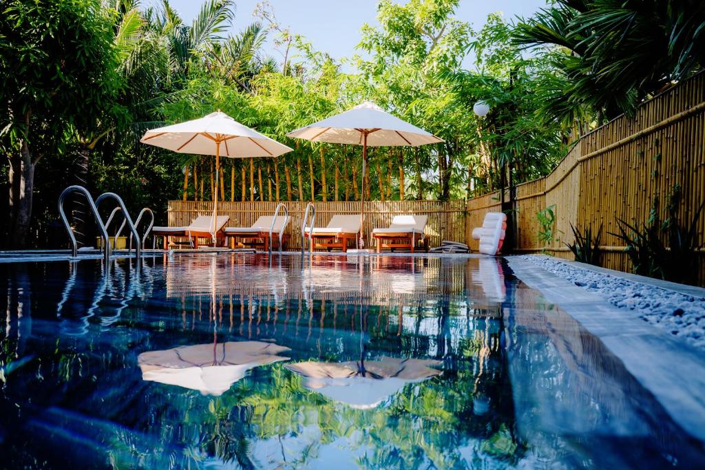 een zwembad met tafels, stoelen en parasols bij RAON Boutique Villa in Hội An