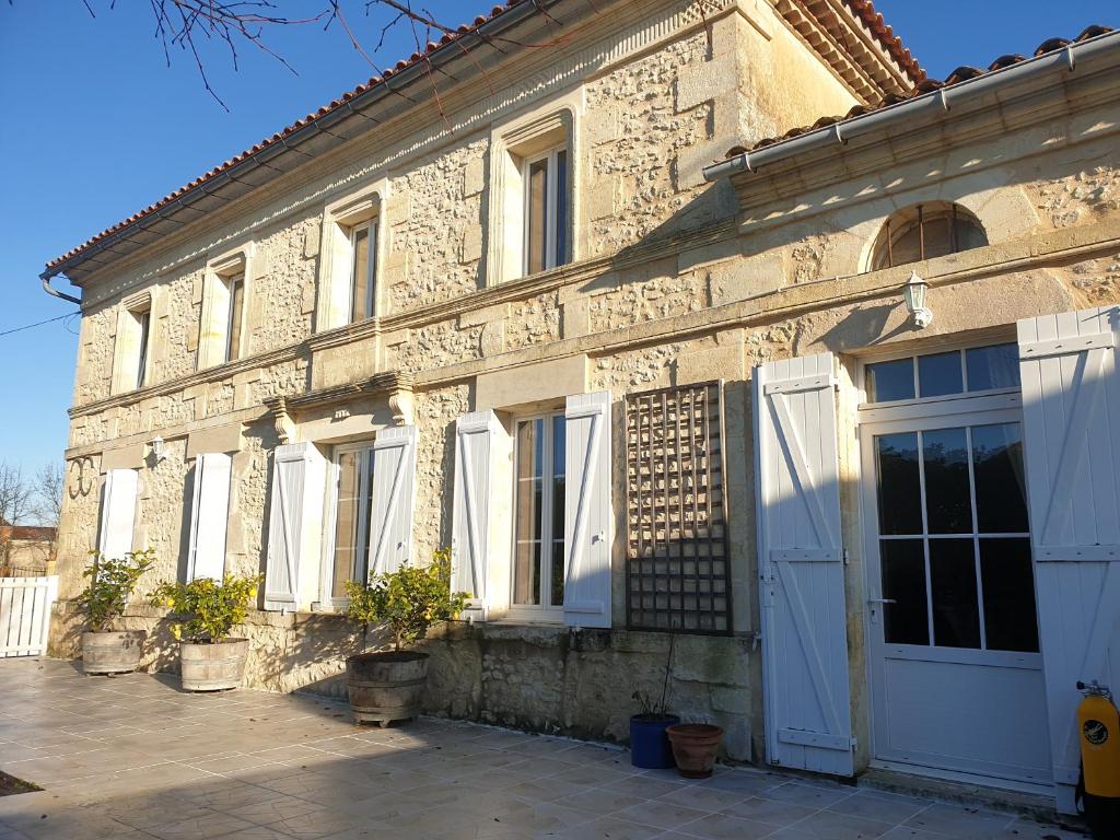 - un vieux bâtiment en pierre avec des portes et des fenêtres blanches dans l'établissement Maison de charme avec suite parentale et grande piscine extérieure, à Anglade