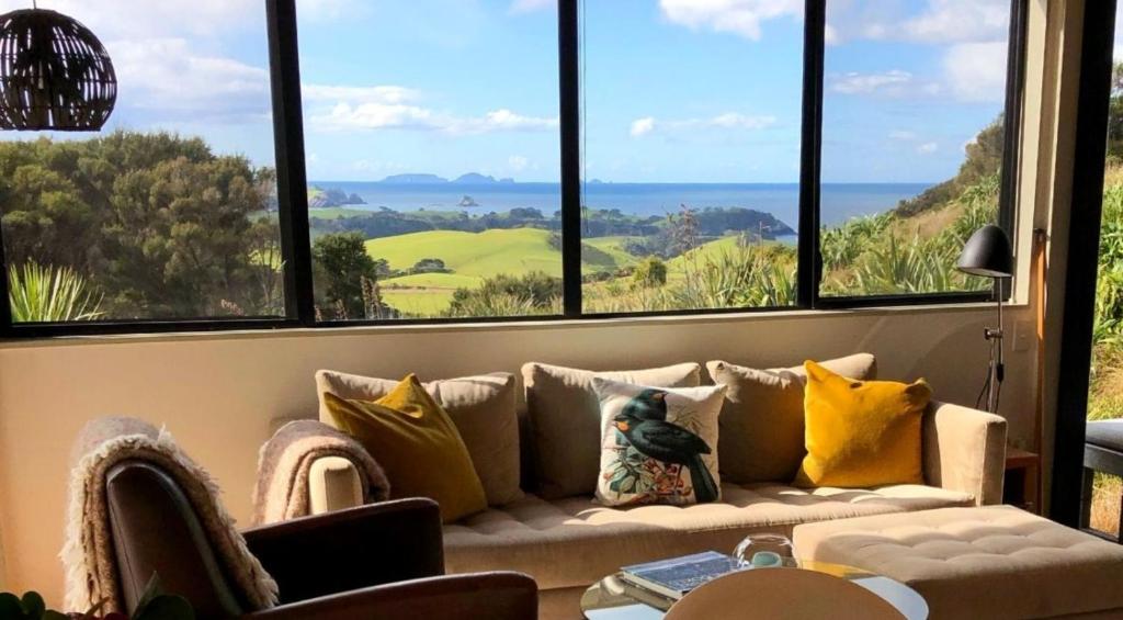 a living room with a couch and large windows at Te Huia in Whangarei Heads