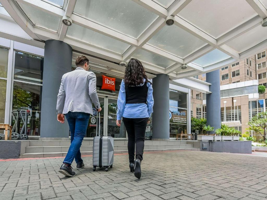 a man and a woman walking down a street with a suitcase at ibis Guarulhos Aeroporto in Guarulhos