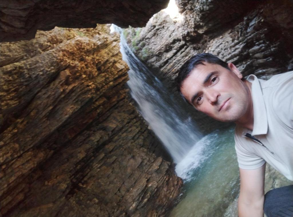 a man sitting in front of a waterfall at Zaur Guest hause in Xınalıq