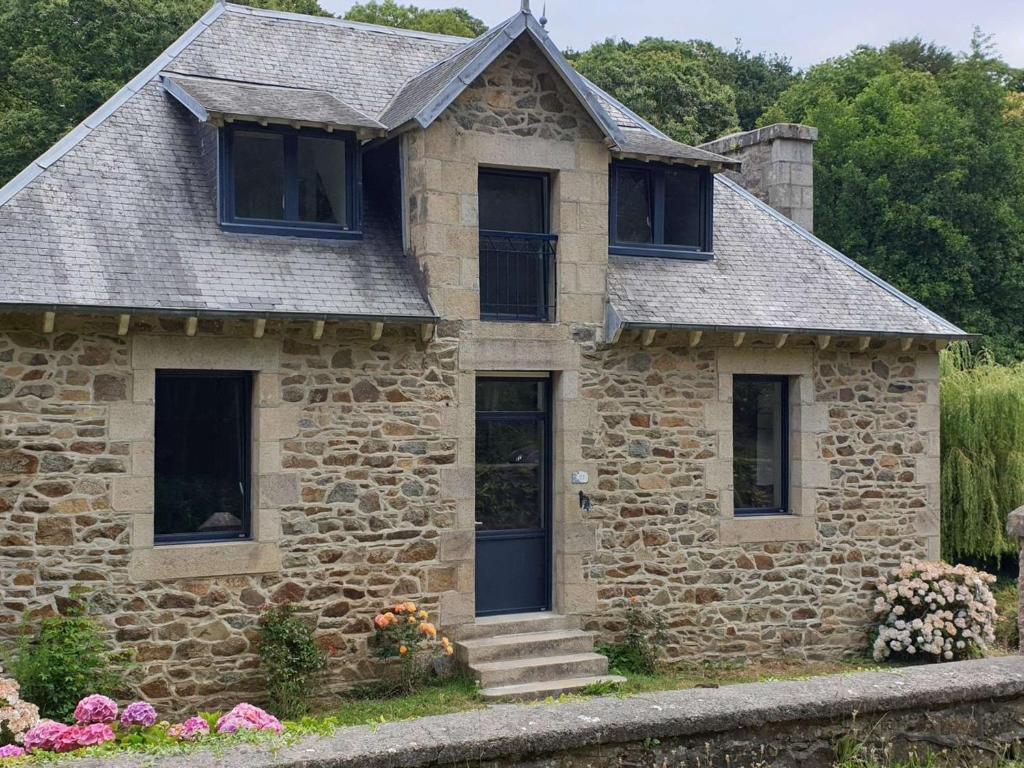 une maison en pierre avec des fenêtres noires et des fleurs dans l'établissement Maison rénovée pierre, jardin, WIFI, 400m mer, St Quay-Perros - FR-1-368-258, à Saint-Quay-Perros