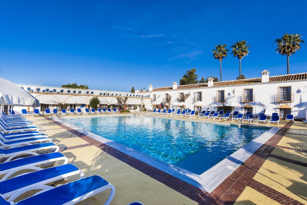 una gran piscina con sillas azules y un edificio en Globales Cortijo Blanco, en Marbella