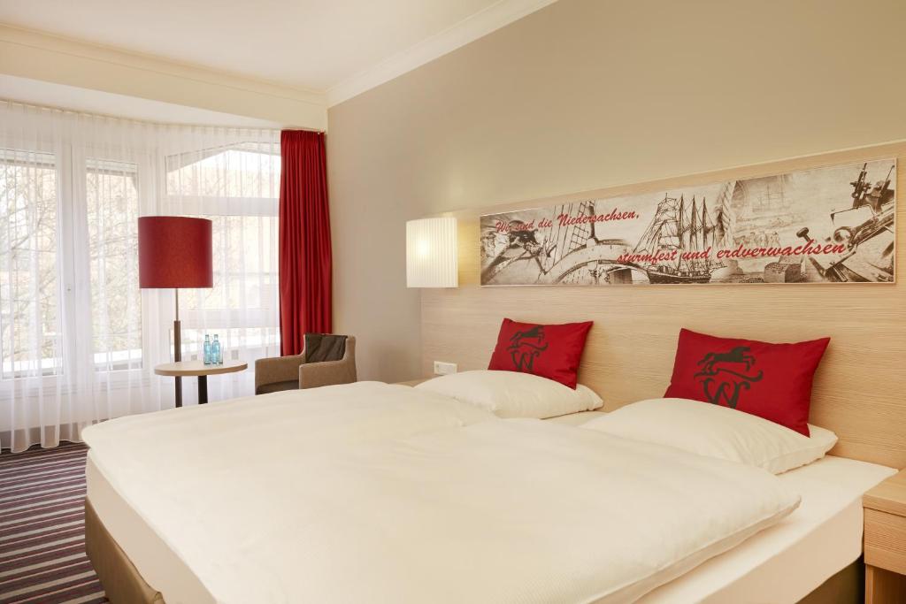 1 dormitorio con 1 cama blanca grande con almohadas rojas en H+ Hotel Stade Herzog Widukind, en Stade